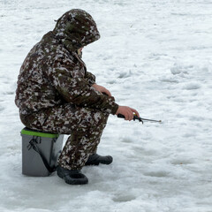 Naklejka premium Man sits on ice, fishing through hole in frozen surface