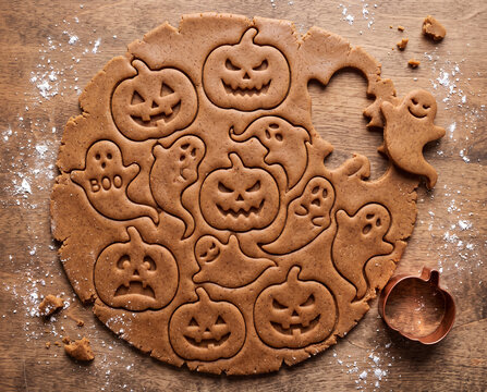 Halloween gingerbread cookie dough with pumpkin and ghost shapes on wooden table