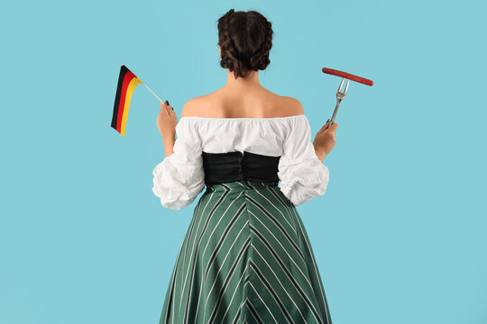 Young Octoberfest waitress with sausage and German flag on blue background, back view