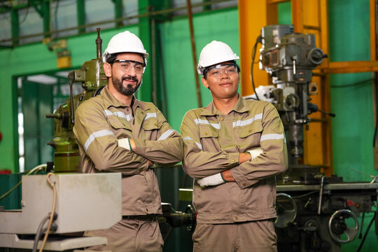 Engineer worker factory helmet uniform industrial machinery safety maintenance portrait team in workshop with crossed arm and confident expression near metal equipment
