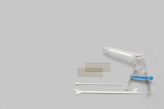 Gynecological speculum with pap smear test tools on grey background