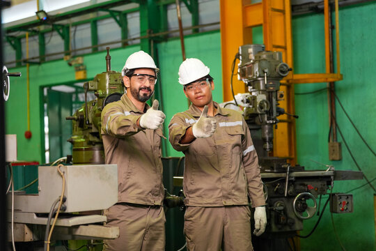 Engineer factory worker hard hat safety uniform machine thumb industrial workshop, two male worker wearing helmet giving thumb gesture in manufacturing workshop with machinery and green wall