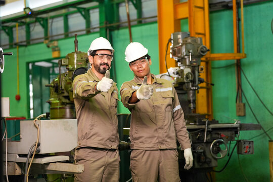 Engineer worker factory hard hat uniform glove thumb machinery workshop industrial portrait of two male staff with positive gesture near equipment