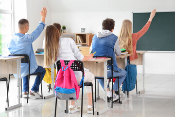 Fototapeta premium Classmates raising hands to answer in classroom