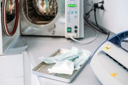 Medical autoclave sits open on countertop near sterilized instruments sealed in protective pouches. Medical sterilization equipment, autoclave sterilization process, instrument disinfection technology