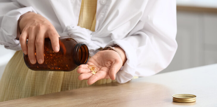 Person pouring omega-3 fish oil capsules from a brown bottle into their hand for daily health supplements