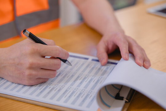Warehouse worker reviewing and signing logistics documents representing inventory management, inspection, paperwork, supply chain operations, quality control industrial business workflow.