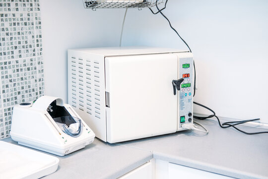 Closed autoclave machine stands on counter in medical sterilization room. Dental sterilization room, autoclave clinic equipment, dental office sterilizer setup.