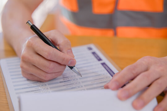 Warehouse worker reviewing and signing logistics documents representing inventory management, inspection, paperwork, supply chain operations, quality control industrial business workflow.