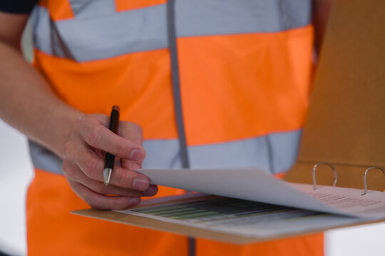 Warehouse worker reviewing and signing logistics documents representing inventory management, inspection, paperwork, supply chain operations, quality control industrial business workflow.