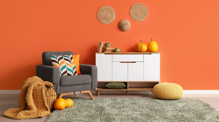 Cozy autumn living room interior with gray armchair, white cabinet, and pumpkins against an orange...