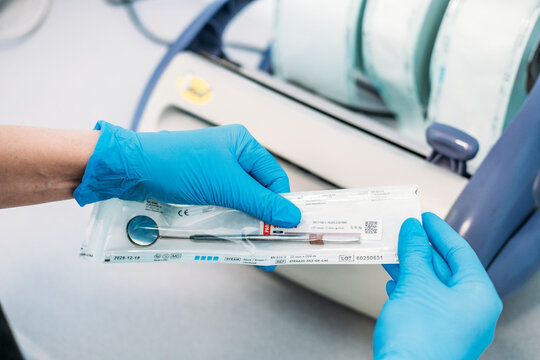 Gloved hands inspect sealed pouches containing dental mirror and probe in clinical environment. Sterilization indicator strip, quality control dental, sterile confirmation label Warsaw, Poland 2026