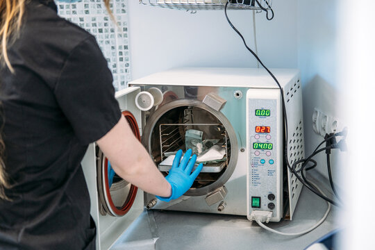 Person closes door of autoclave sterilizer machine in medical facility. Dental sterilization equipment, clinical device closeup, medical machinery technology detail.