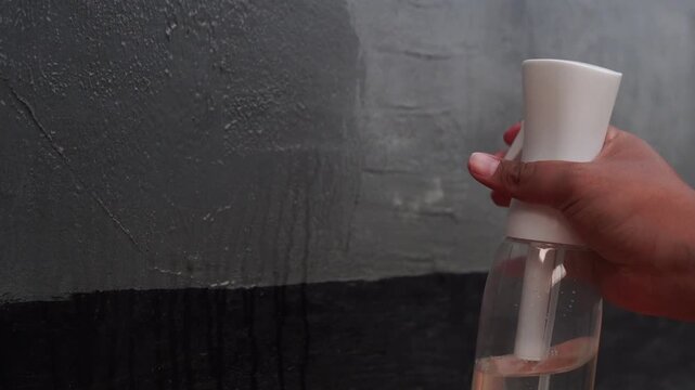 an anonymous hand spraying liquid onto a rough concrete wall.