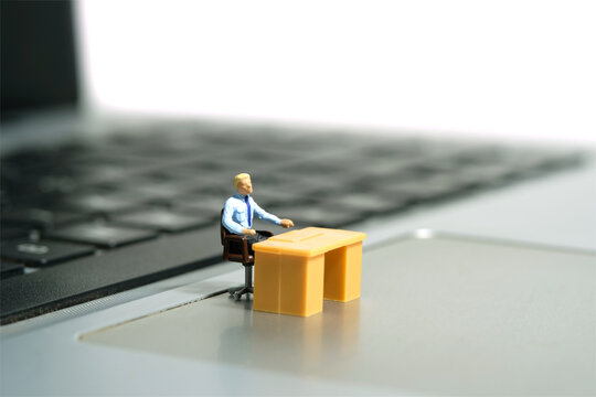 Miniature tiny people toy figure photography. A tired businessman seat in the desk, stunned above notebook