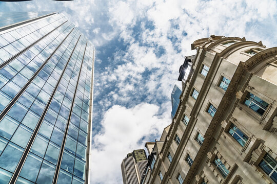 View of the City of London featuring a modern glass skyscraper contrasting with a historic stone building under a blue sky with clouds in London, England, United Kingdom.