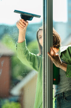 Cleaner washing window with squeegee at home during summer