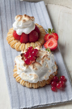 Two meringue tartlets with red currants and strawberries on wood, studio shot