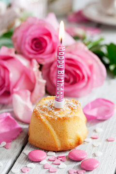 Muffin with lighted birthday candle, baking decor and pink roses on table