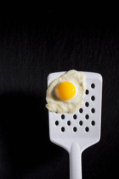 Fried quail egg on egg lifter in front of dark background