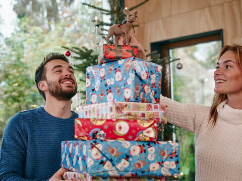 man carrying stack of Christmas presents, woman putting reindeer on top