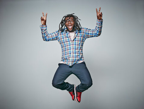 Screaming man with dreadlocks jumping in the air while showing victory signs