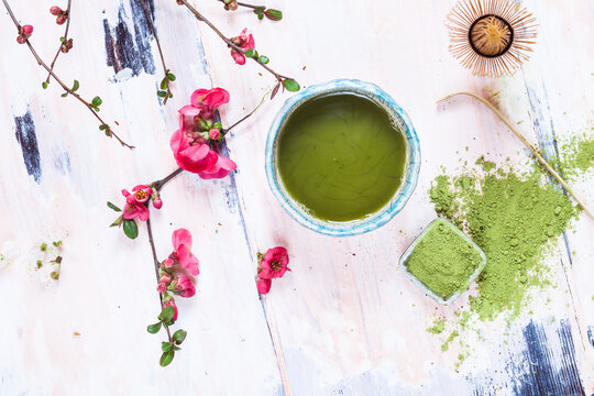 Matcha tea in bowl, with match powder, spoon and chasen and pink flowers
