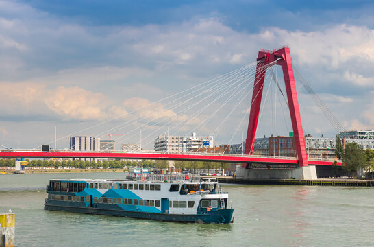 Passenger boat sails along the Nieuwe Maas river past the red Willemsbrug bridge in Rotterdam, Netherlands