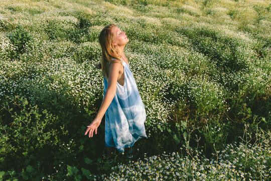 Woman in dress enjoys freedom standing in a chamomile field
