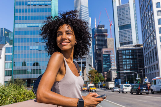 Germany, Frankfurt, portrait of smiling young woman with curly hair in the city