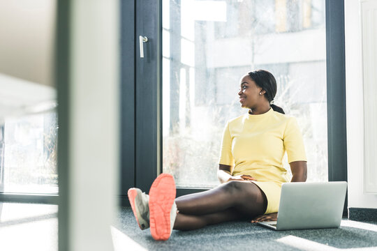 Businesswoman sitting at the window in office using laptop