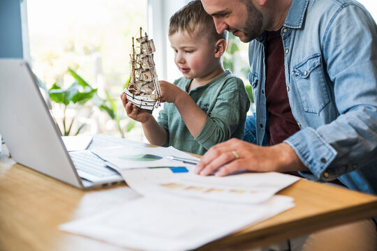 Father works at home while his son plays with a toy ship