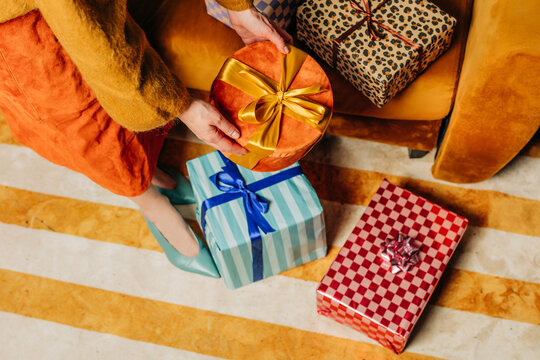 Woman unwraps a festive holiday gift standing next to a yellow couch