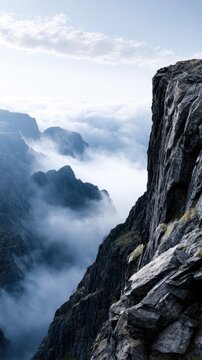 Majestic rugged rocky mountain cliffs rising above dense swirling mist and clouds under a clear sky at sunrise or sunset