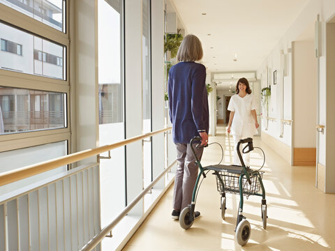 A woman with a walking frame meets a nurse in a nursing home corridor