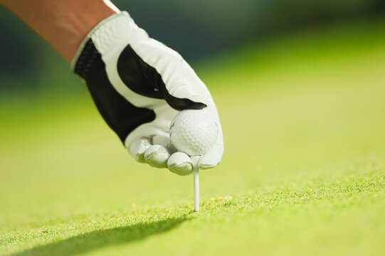 A male hand places a golf ball on a tee at a golf course in Italy