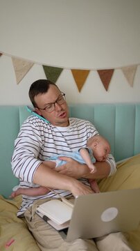 Young freelance father multitasking while holding his newborn son, talking on the phone and working on a laptop, struggling with the challenges of paternity leave