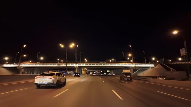 Night urban freeway beneath illuminated interchange with cars and freight truck