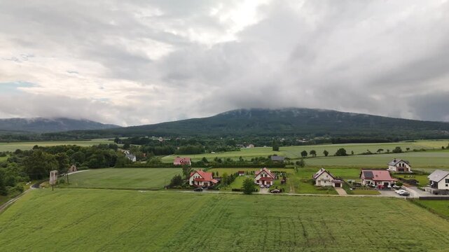 Aerial view of houses and fields on a plain with cloud covered mountains in the background in summer