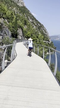 Woman in blue shirt and straw hat cycling on a mountain bike path near Lake Garda, Italy
