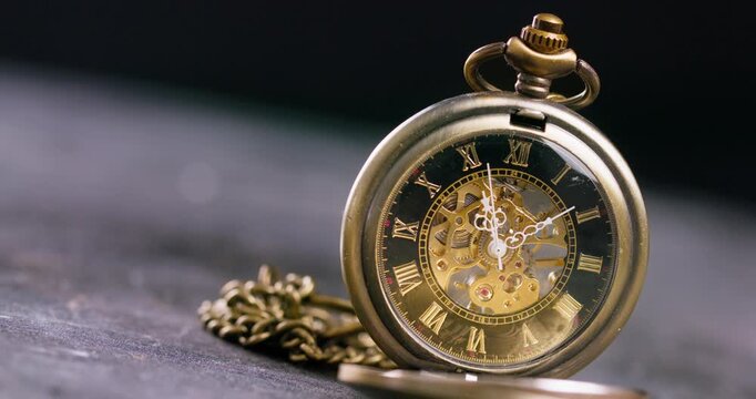 An antique pocket watch with intricate gears and a vintage design resting on a dark.