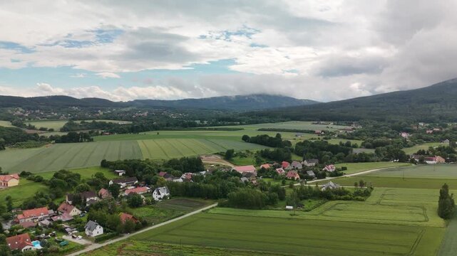 Aerial View of a Village Among Green Fields with Cloud Covered Mountains in the Distance