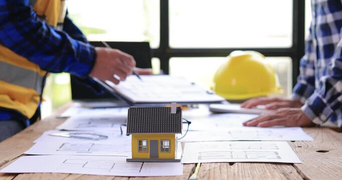 Two construction professionals discussing plans at a table with a small model house.