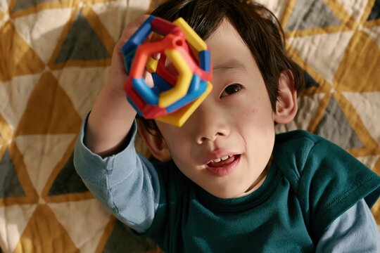 Preschool boy reaching up with geometric rattle on patterned quilt for play activity background and toddler engagement banner