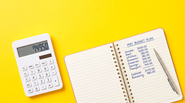 Personally written May budget plan with calculator and pen on bright yellow background