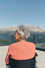 Fototapeta premium Rear view of elderly woman in wheelchair on balcony with distant mountain vista for senior care banner and peaceful background design