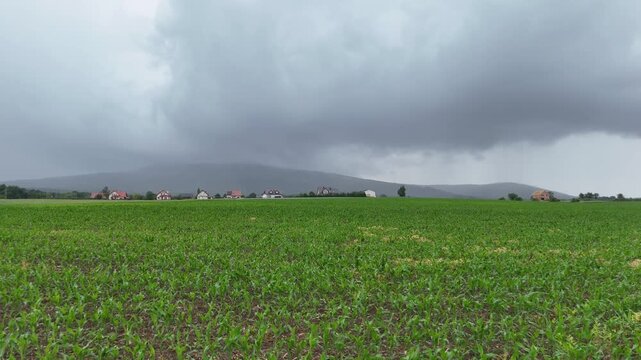 Storm clouds over green crop field and village near Ślęża mountain, Poland