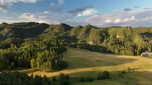 Aerial view of forested sandstone hills and golden meadow at sunset in Bohemia, Czech Republic