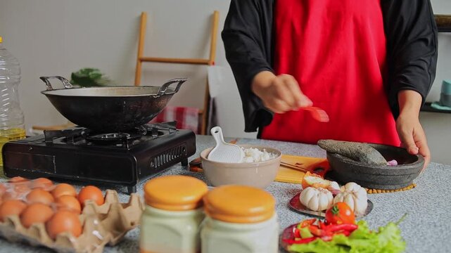 Chef hand in apron prepares ingredients and crushes garlic using stone mortar and pestle in kitchen