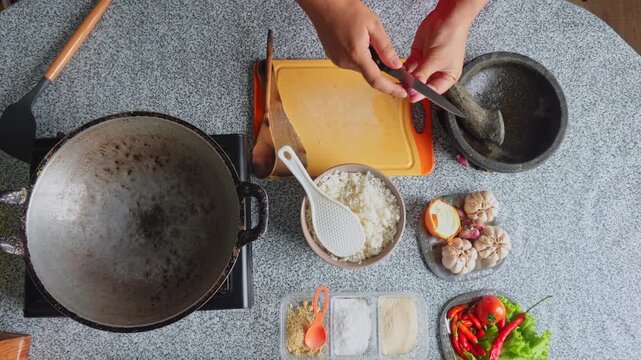 Top-down view of chef peeling shallots next to fresh ingredients to make Indonesian fried rice